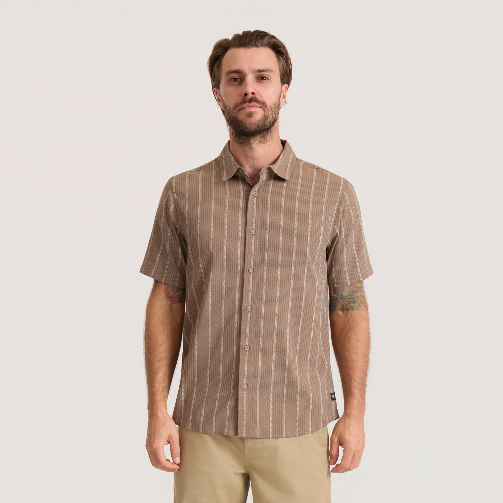 Tan striped short-sleeve button-up shirt on male model wearing khaki pants against neutral background